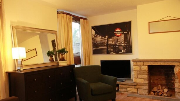 Una sala de estar con un aparador de madera oscura, un sillón verde, un televisor de pantalla plana, una chimenea y un cartel del metro de Londres en la pared.