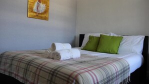 Una cama bien hecha con colcha escocesa, almohadas verdes y un cuadro de una bailarina en la pared.