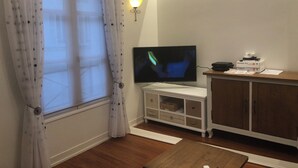 Una sala de estar con televisor, aparador, lámpara y ventana con cortinas.