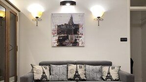 Una sala de estar con un sofá gris, una mesa de centro de madera y un cartel con un paisaje urbano en la pared.