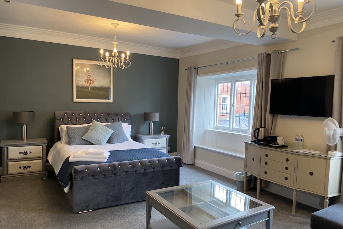 A bedroom with a bed, bedside tables, a TV, a glass coffee table, and a window with curtains.