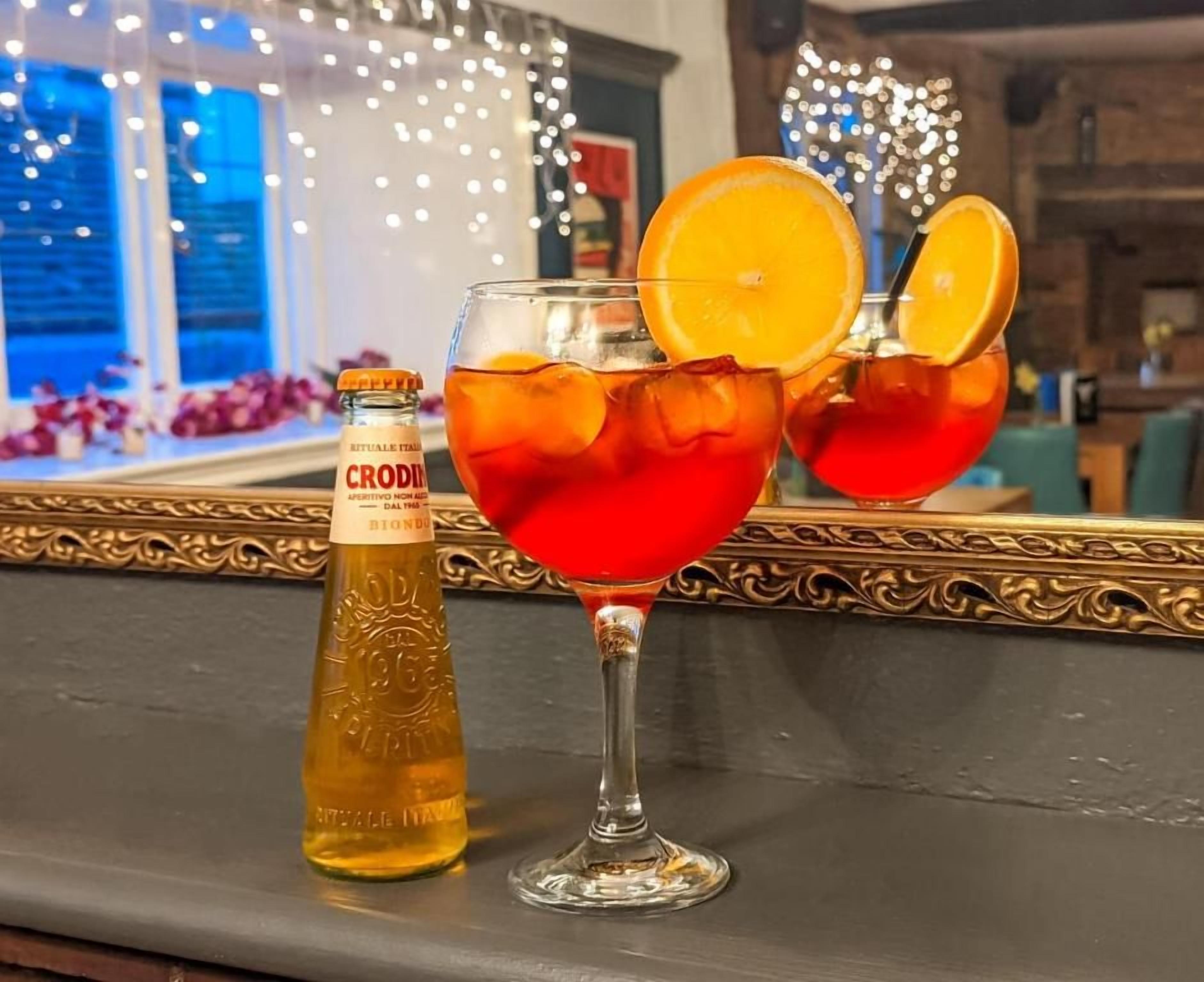 Un bar con una botella de Croci y dos vasos de una bebida roja, posiblemente un cóctel, con rodajas de naranja.