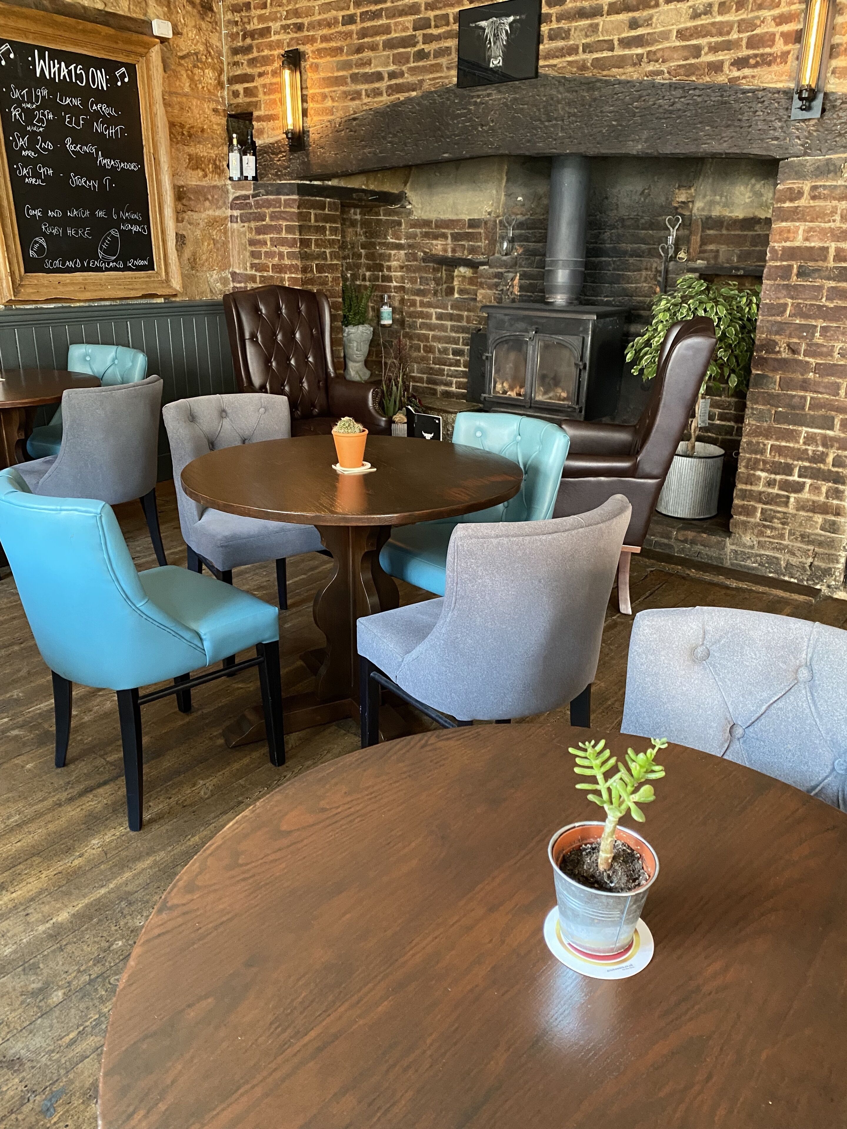 A cozy pub with a brick wall, a fireplace, and a chalkboard menu.
