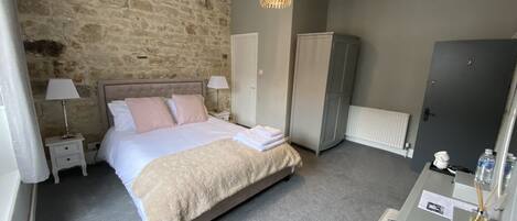 Ein Schlafzimmer mit einer Steinsturz, einem Bett mit einer beigen Decke, einem Kleiderschrank, einem Schreibtisch mit einem Computer und einer Lampe.