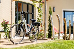 A bicycle parked outside a building with a covered patio area, a potted plant, and a wooden fence. - La Maison du Grand Bossieu (Bossieu)
