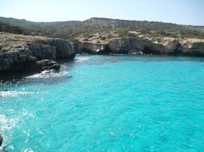 A coastal scene with clear turquoise water, rocky cliffs, and a hilly landscape in the background. - Modern Apartment Near the Beach in Cyprus (Polis)
