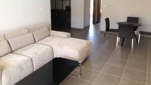 A modern living room with a beige sectional sofa, a black coffee table, and a dining area with a small table and chairs. - Modern Apartment Near the Beach in Cyprus (Polis)
