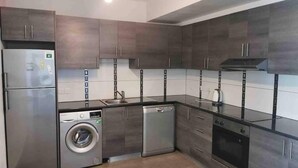 A modern kitchen with dark cabinetry, stainless steel appliances, and a built-in washer and dryer. - Modern Apartment Near the Beach in Cyprus (Polis)