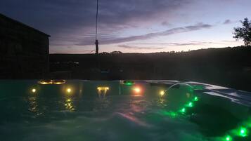 A hot tub with green and yellow lights, surrounded by a stone wall and a view of the sky.