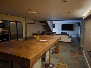 A modern kitchen with a wooden island, built-in appliances, and a dining area with a staircase leading to a living room. - Green Barn (Sheffield)