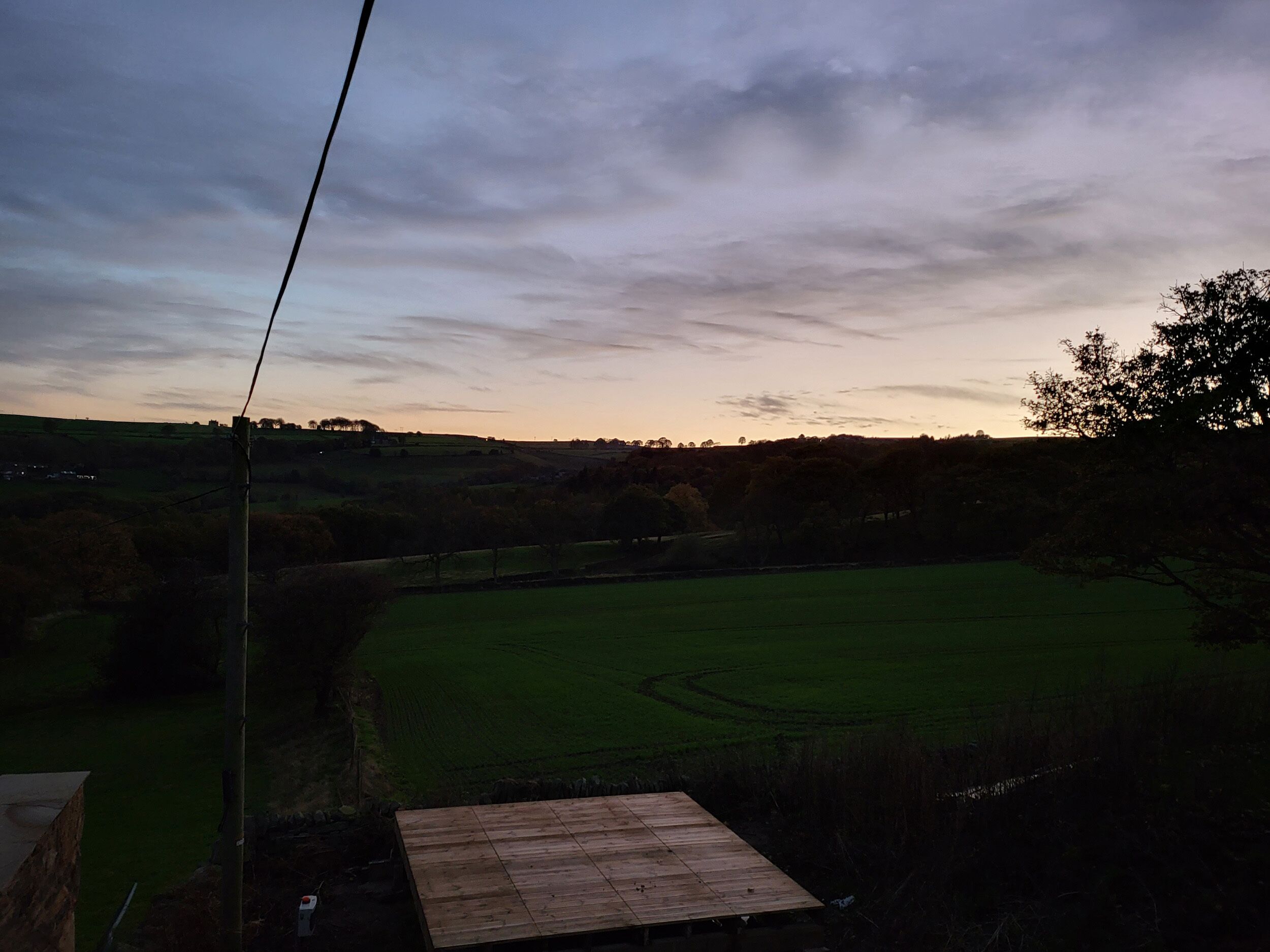 Una terraza de madera con vistas a un campo verde bajo un cielo nublado.