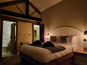 A bedroom with a wooden headboard, a large bed with white bedding, a nightstand, and a wall-mounted light fixture. - Green Barn (Sheffield)