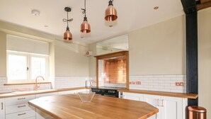 Una cocina moderna con una isla central, armarios blancos, detalles en cobre y un ventanal grande.
