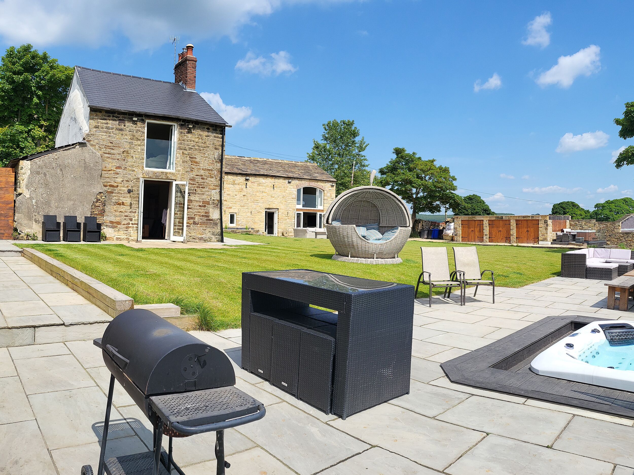 A stone house with a grassy yard, outdoor seating, a hot tub, and a barbecue grill.