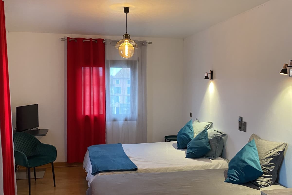 A modern bedroom with a large bed, two bedside tables, a TV, and a red curtain.