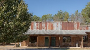 A rustic building with a corrugated metal roof and wooden walls, featuring a front porch with benches. - Southern Comfort Cabin- minutes from the river and the lake! (Murfreesboro)