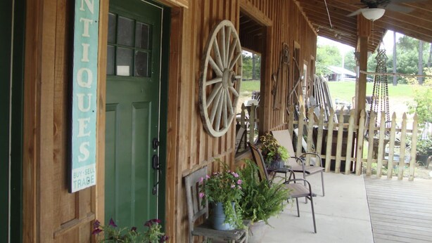 A rustic wooden building with a green door, a sign reading "ANTIQUE TRADE", and a porch with chairs and potted plants. - Southern Comfort Cabin- minutes from the river and the lake! (Murfreesboro)