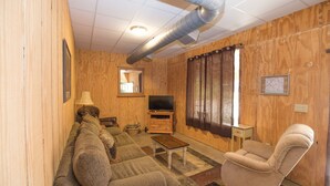 A cozy living room with a sofa, armchair, TV, and a fireplace. - Southern Comfort Cabin- minutes from the river and the lake! (Murfreesboro)