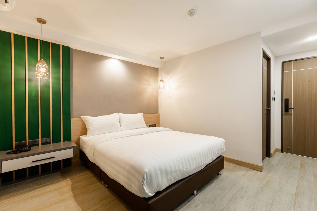 A modern bedroom with a large bed, bedside tables, a green accent wall, and a wooden wardrobe.