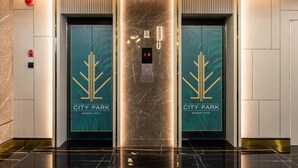 Un ascenseur moderne doté d’un écran numérique et d’un bouton d’urgence, encadré par des portes arborant le logo « CITY PARK ».