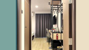 A hotel room with a wooden floor, a desk with a chair, a mirror, and a wardrobe.