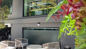 Un espace extérieur aménagé avec des chaises et des tables en osier, un bâtiment moderne doté de grandes fenêtres et un logo bien visible sur la vitrine.