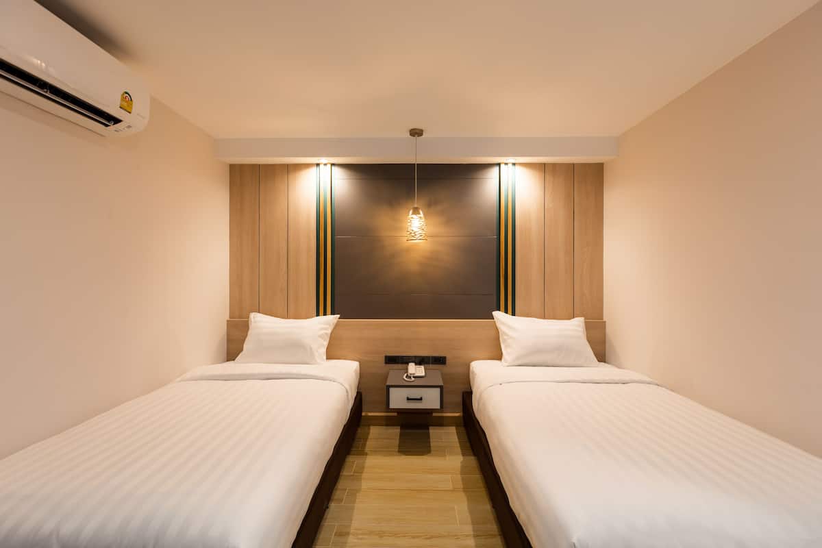 A modern hotel room with two single beds, a wooden headboard, a nightstand with a phone, and a hanging light fixture.