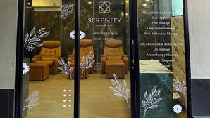 Un spa doté d’une porte en verre, de fauteuils de massage à l’intérieur et d’un panneau indiquant les services proposés, tels que les massages thaïlandais et l’aromathérapie.