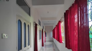 A corridor with red curtains, a marble floor, and a window with a metal grille. - Homecation Manas River Rock Lodge (Barnagar)