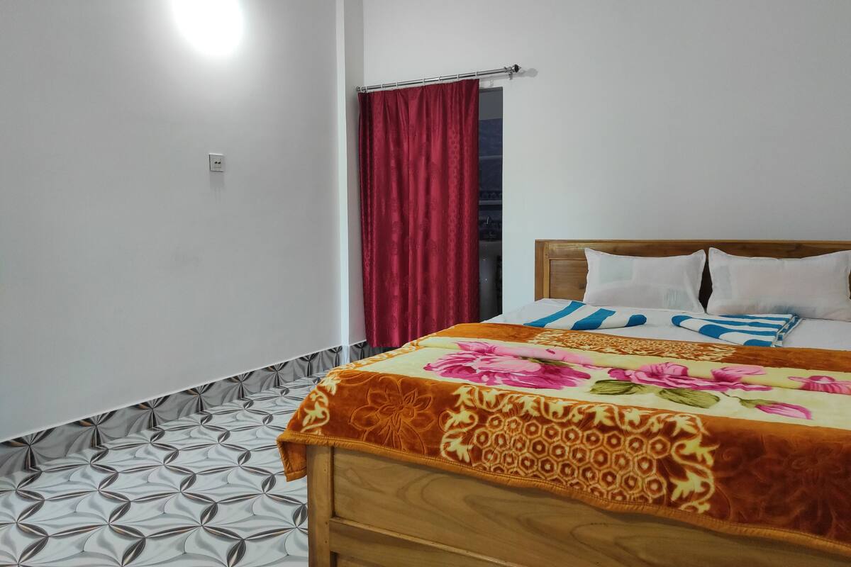 A bedroom with a bed, a wooden headboard, a red curtain, and a patterned floor.
