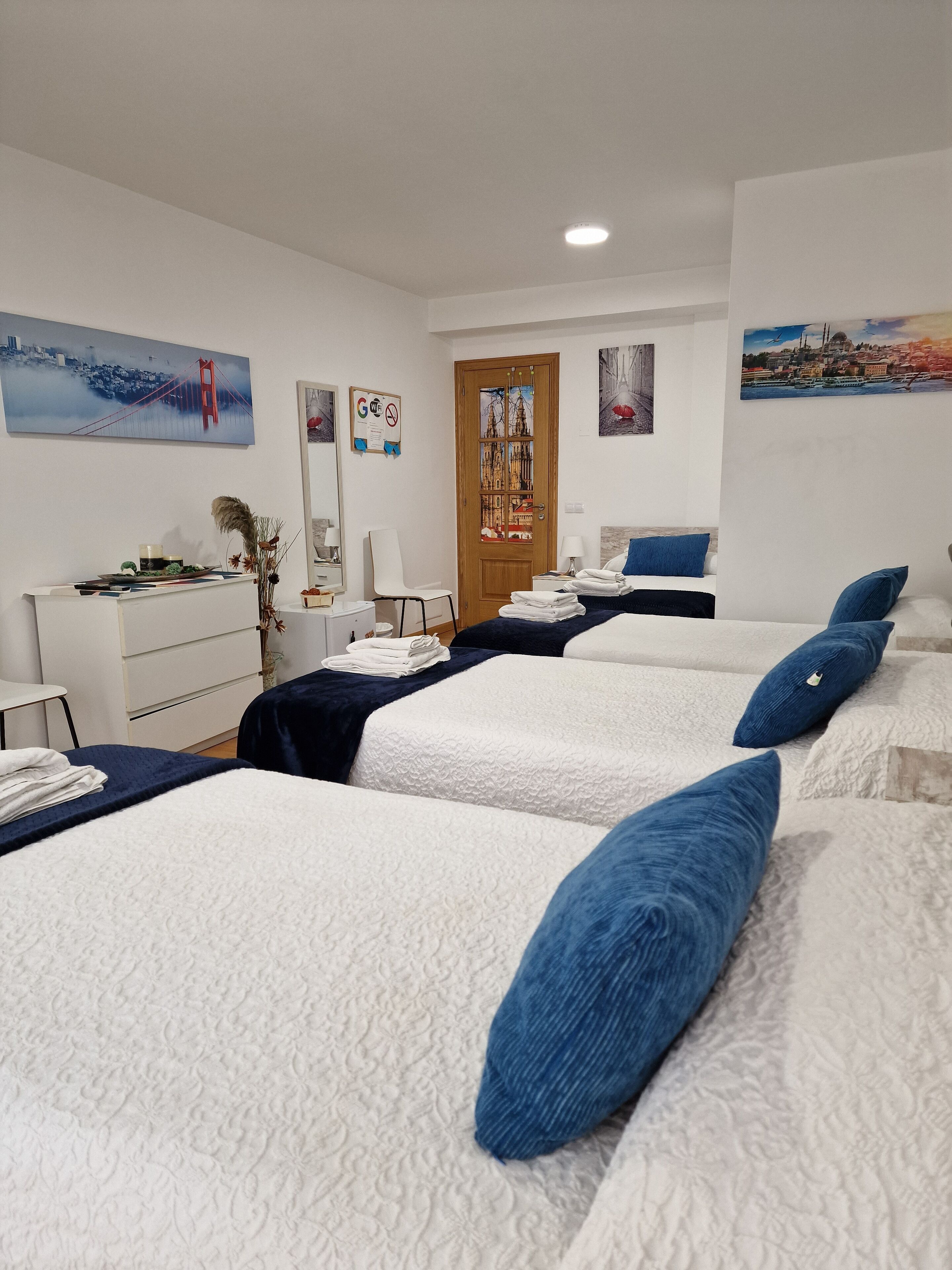 A hotel room with three beds, a desk, a chair, and a door with a glass panel.