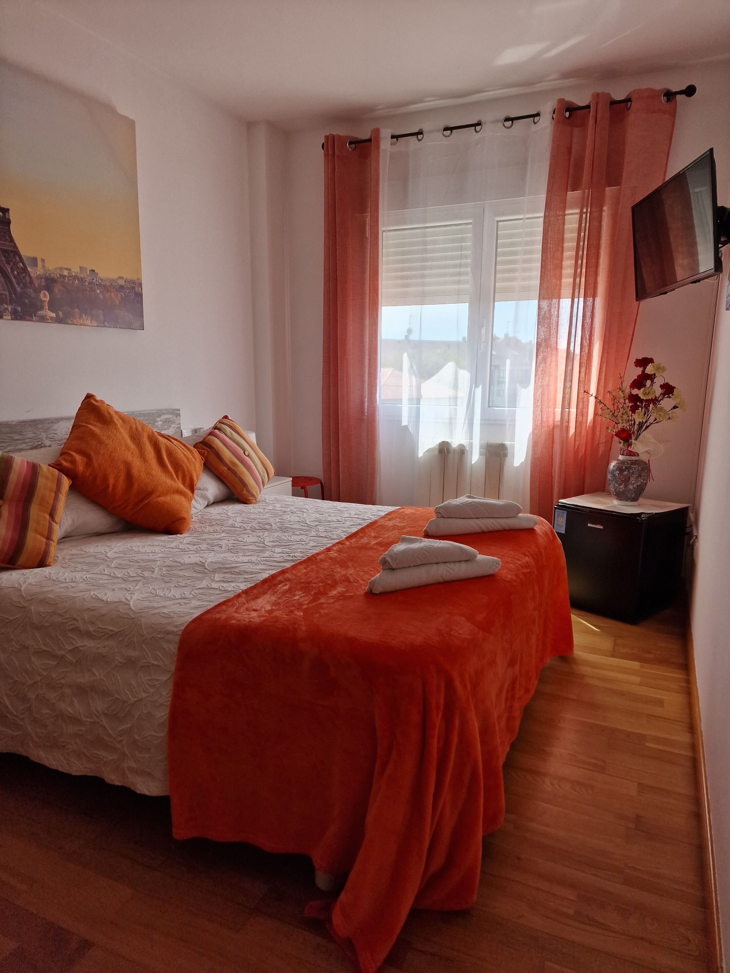 Una camera da letto ordinata con un letto, cuscini, un comodino con un vaso e una finestra con tende.