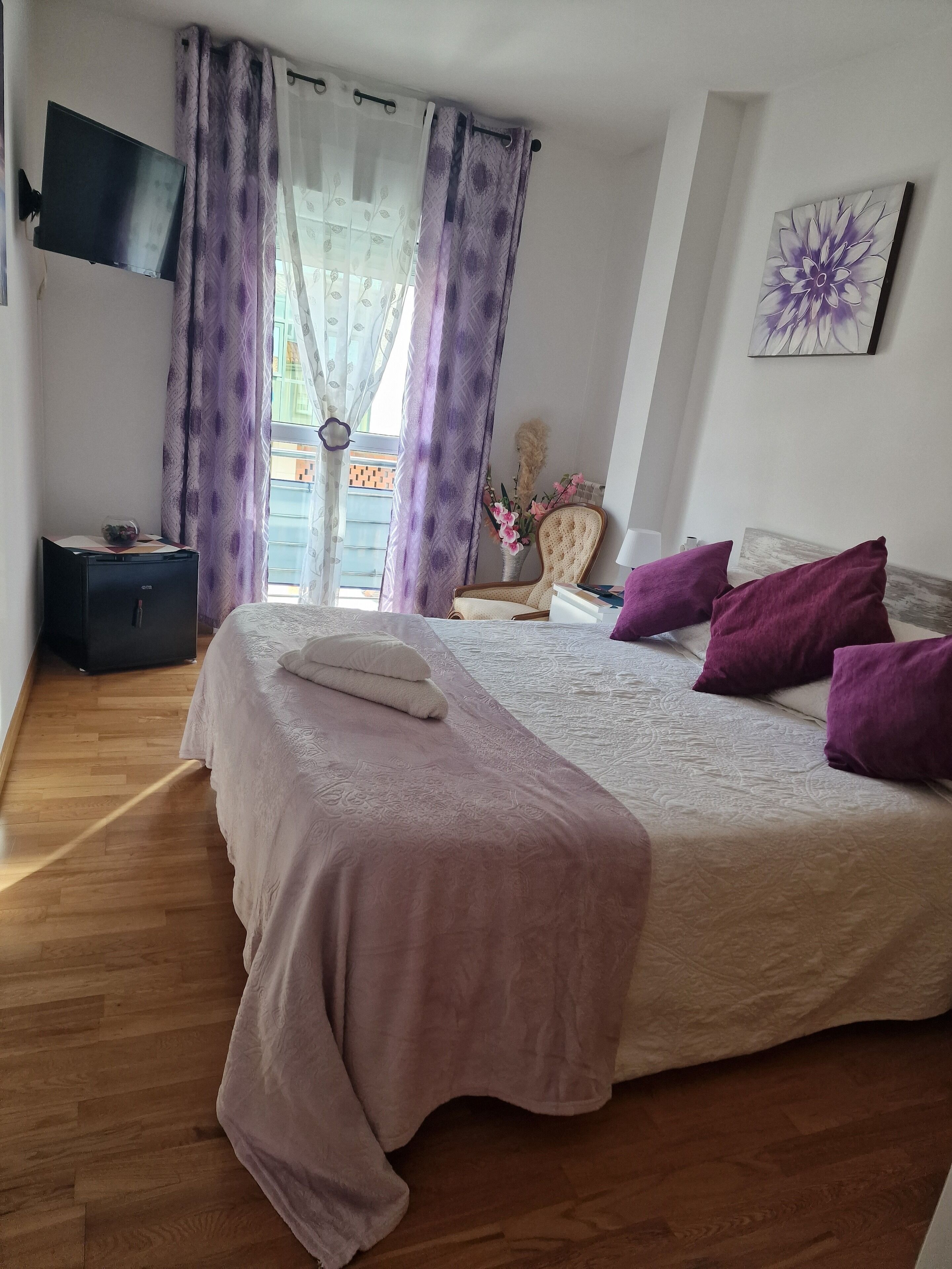 A bedroom with a bed, a TV, a chair, and a window with curtains.