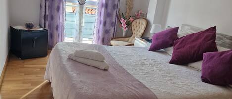 A bedroom with a bed, a TV, a chair, and a window with curtains.