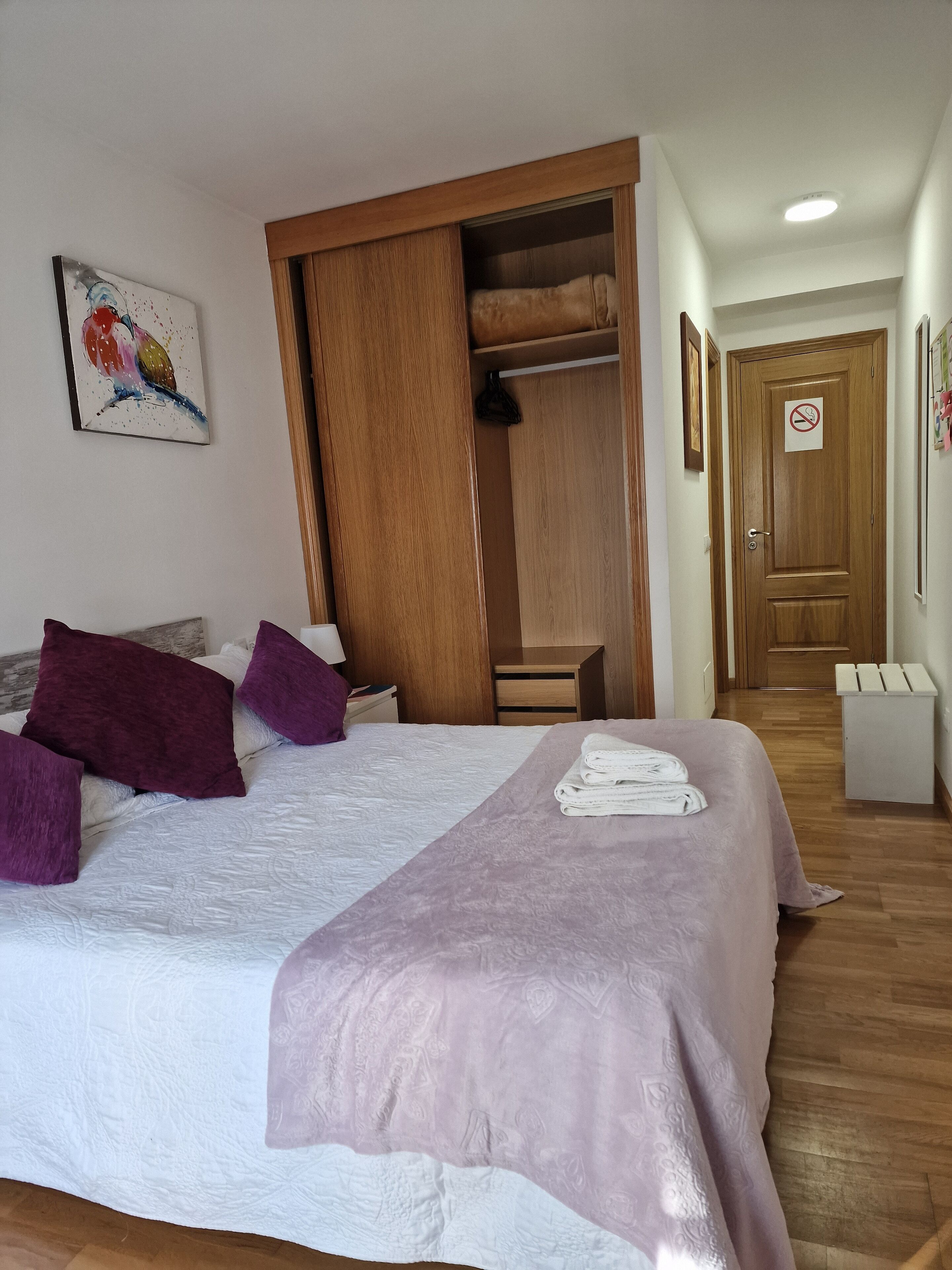 Une chambre à coucher avec un lit, une armoire, une porte sur laquelle est apposé un panneau « interdiction de fumer » et un couloir.