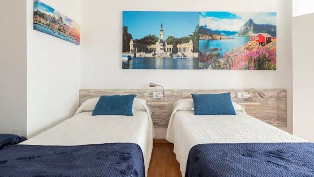 A hotel room with two single beds, a large painting of a coastal scene, and a wooden headboard. - Pensión Myrian (O Pino)
