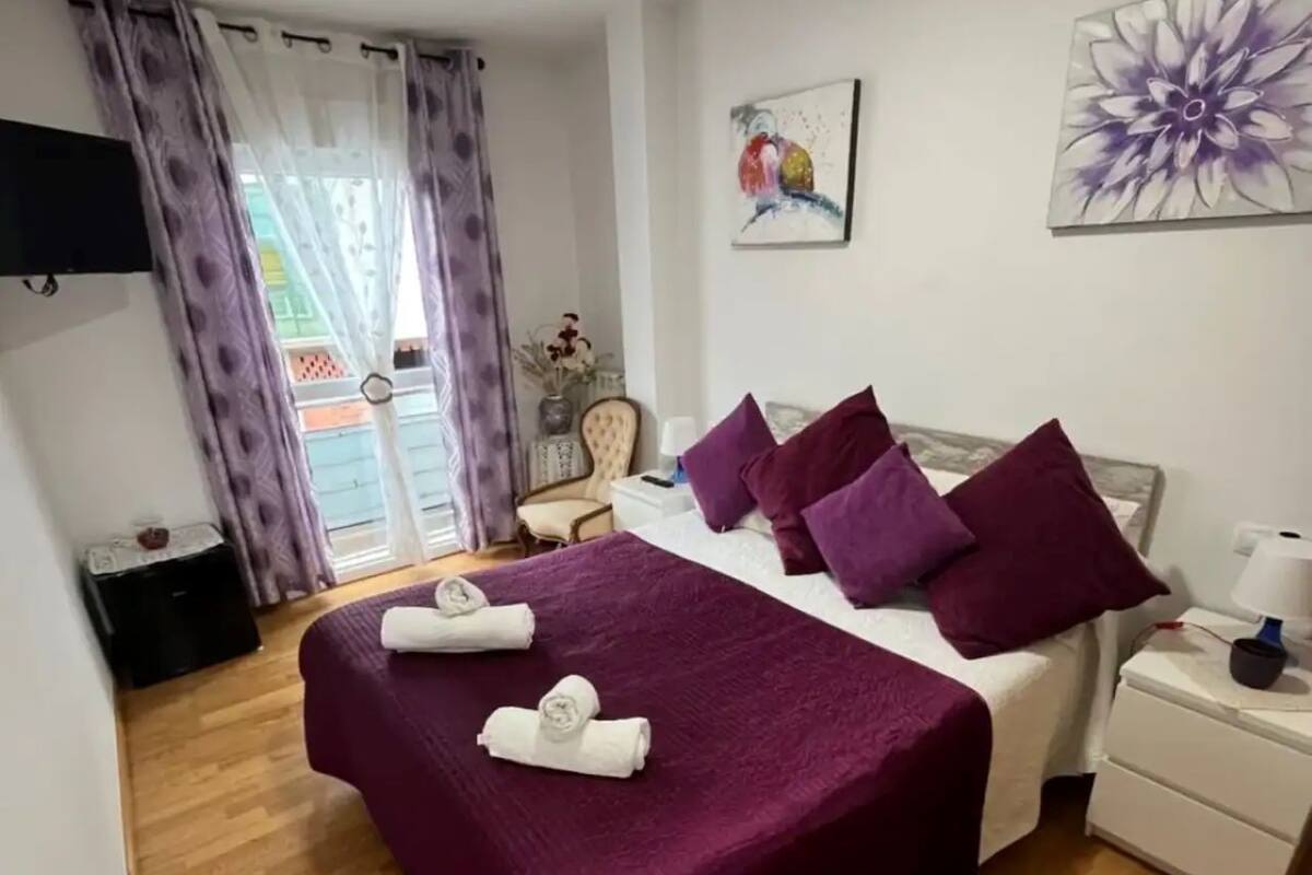 A bedroom with a large bed, purple bedding, and two towels on the bed.