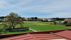 A red roof with a clear view of a green field and houses in the distance. - Pensión Myrian (O Pino)