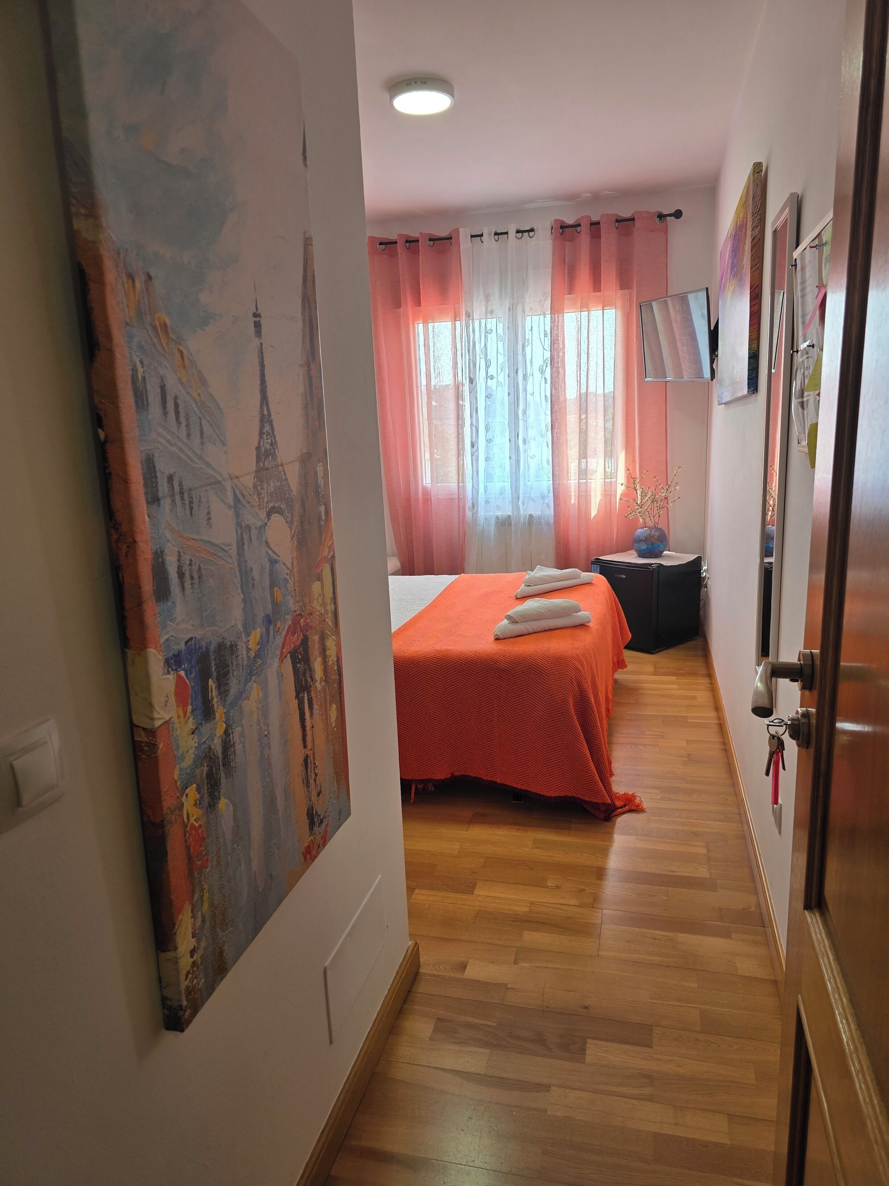 Habitación de hotel con cama, escritorio, silla, un cuadro y ventana con cortinas.