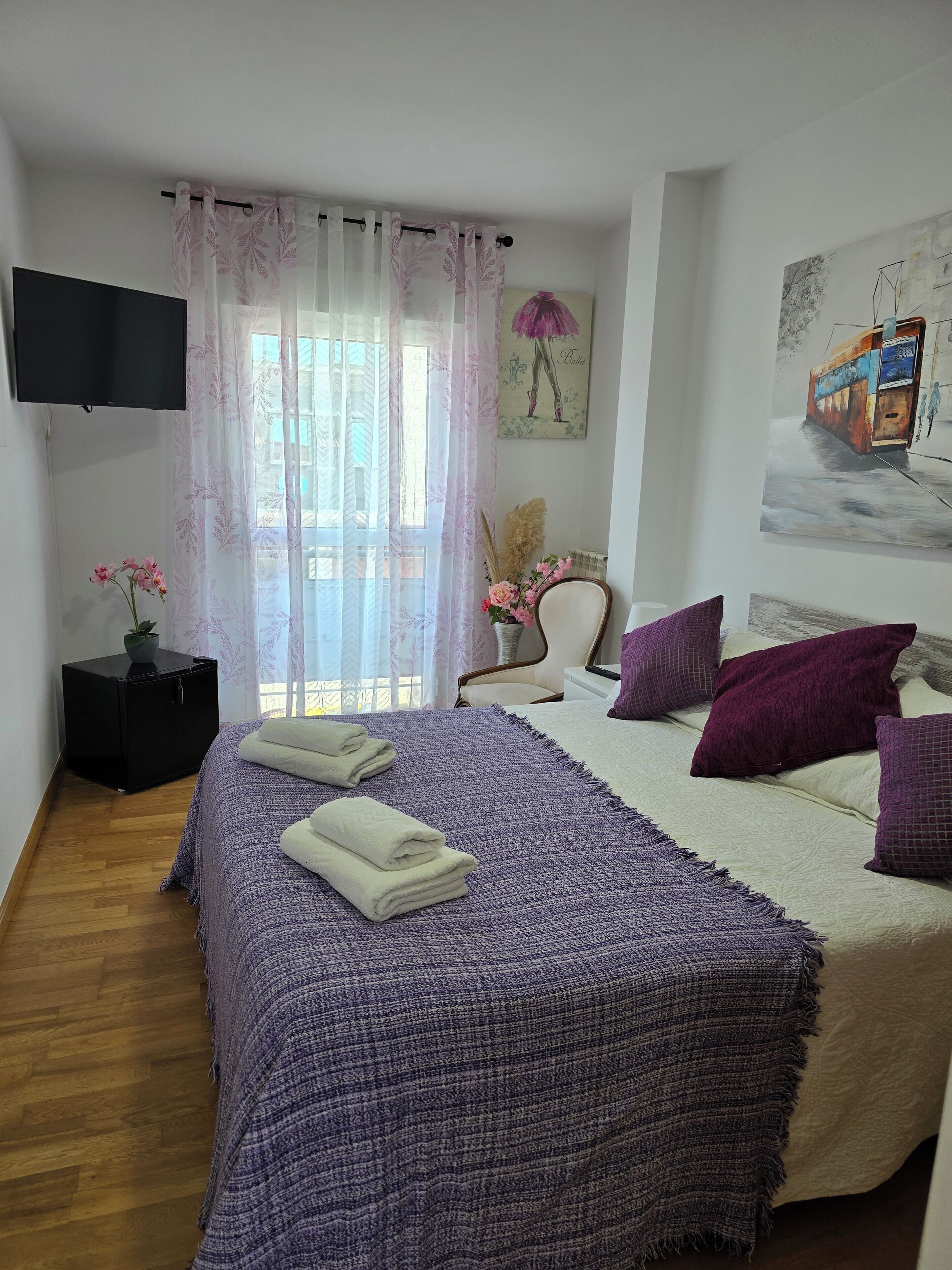 A bedroom with a bed, a chair, a TV, and a painting on the wall.