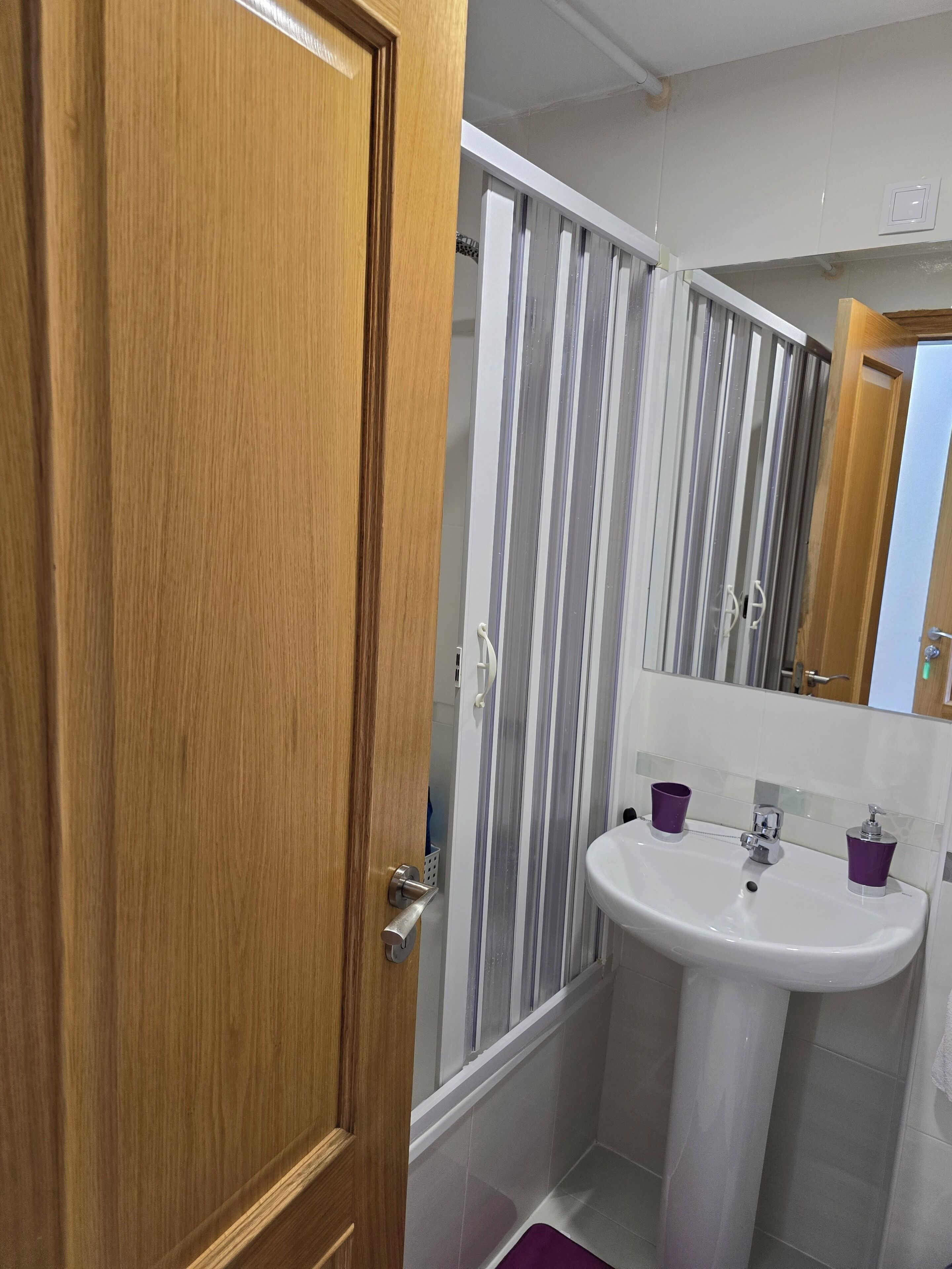 A bathroom with a wooden door, a striped shower curtain, a white sink, and purple cups.