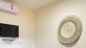 A room with a bed, a television mounted on the wall, and a woven basket on the wall.