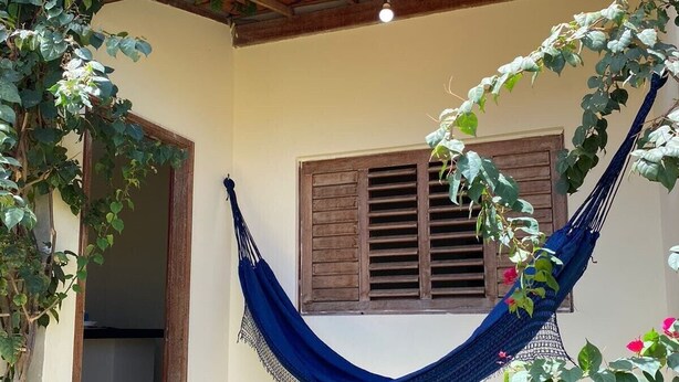 A hammock under a wooden pergola, a wooden door, and a window with shutters.