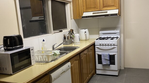 Una cocina compacta con armarios de madera, un microondas, un tostador, una tetera, un fregadero y una estufa.