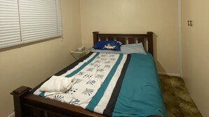 Un dormitorio con una cama de madera, una mesita de noche, un ventilador de techo y una ventana con persianas.