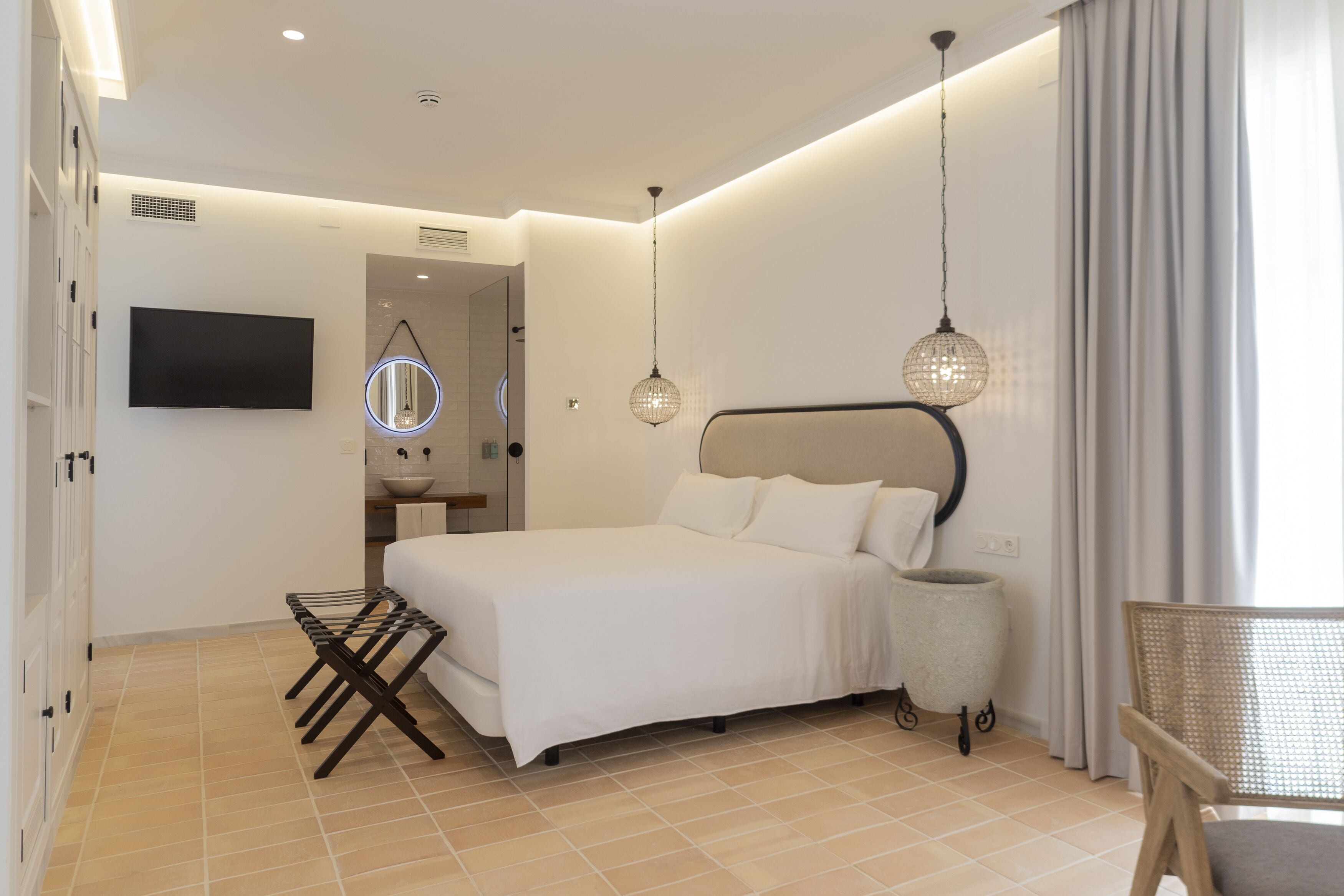 Un dormitorio moderno con una cama grande, televisión, mesita de noche, lámpara y una silla.