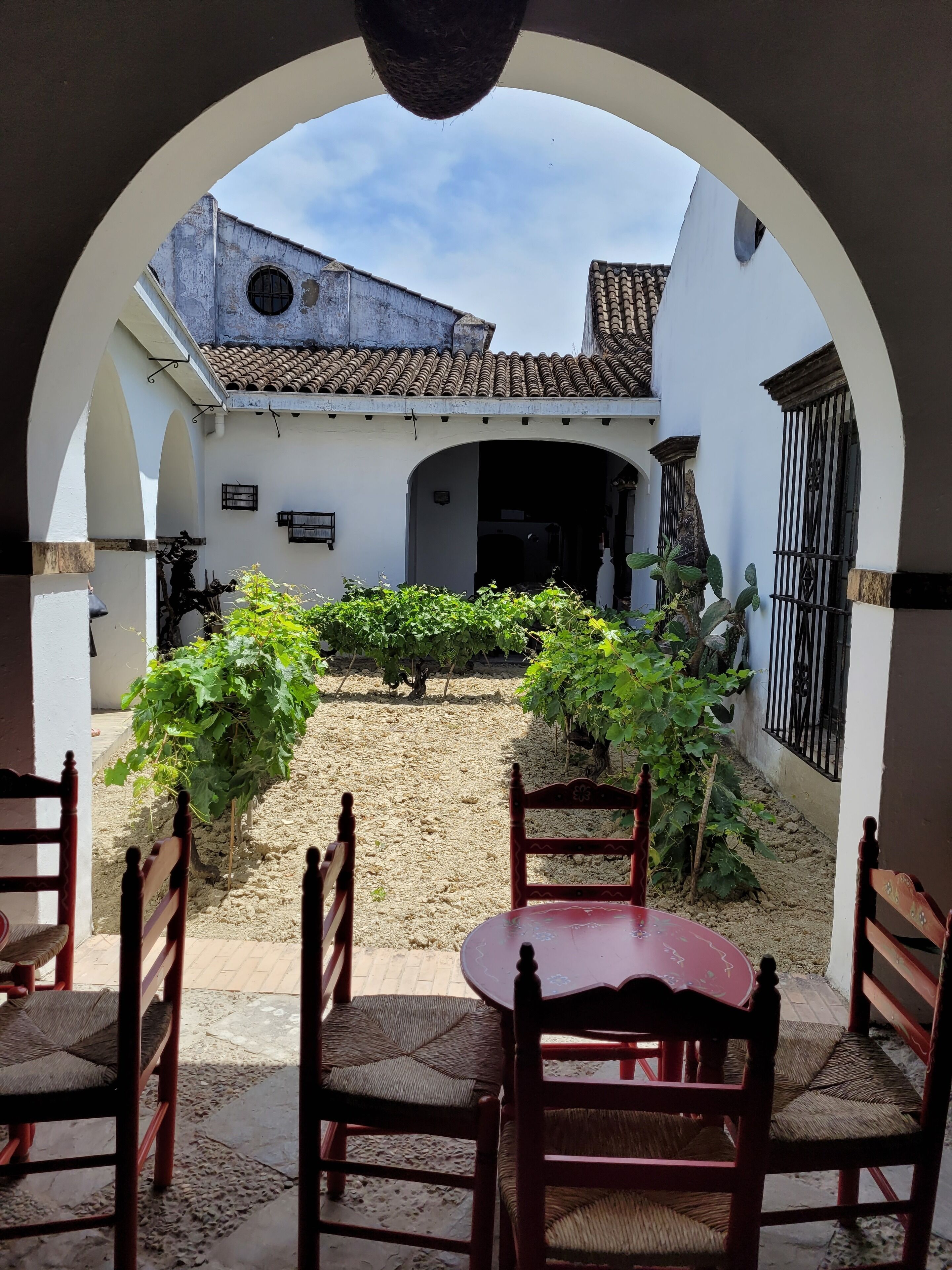 Une cour avec une table et des chaises, entourée de murs blancs et surmontée d’un toit en tuiles.