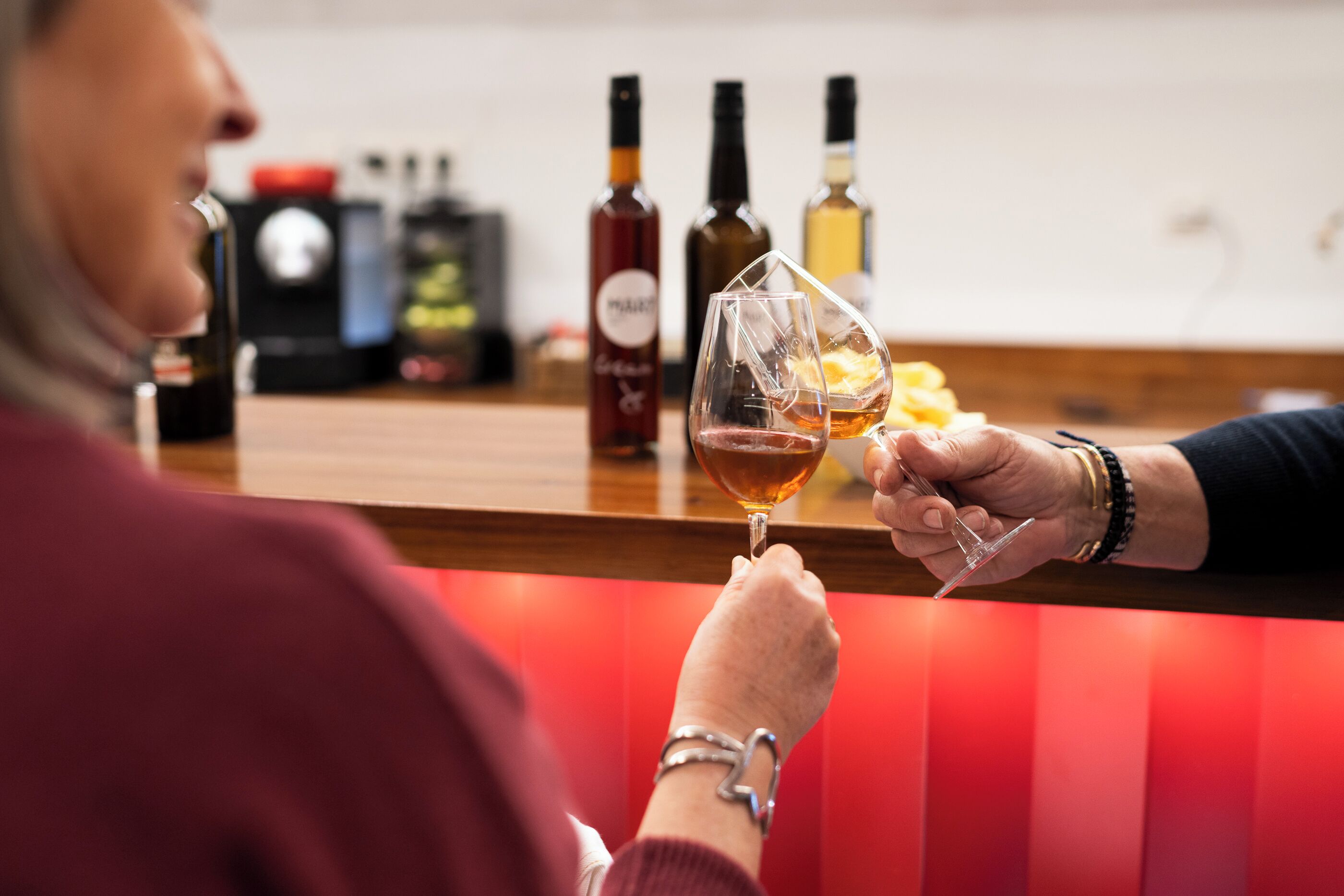 A person holding a wine glass at a bar with bottles in the background.
