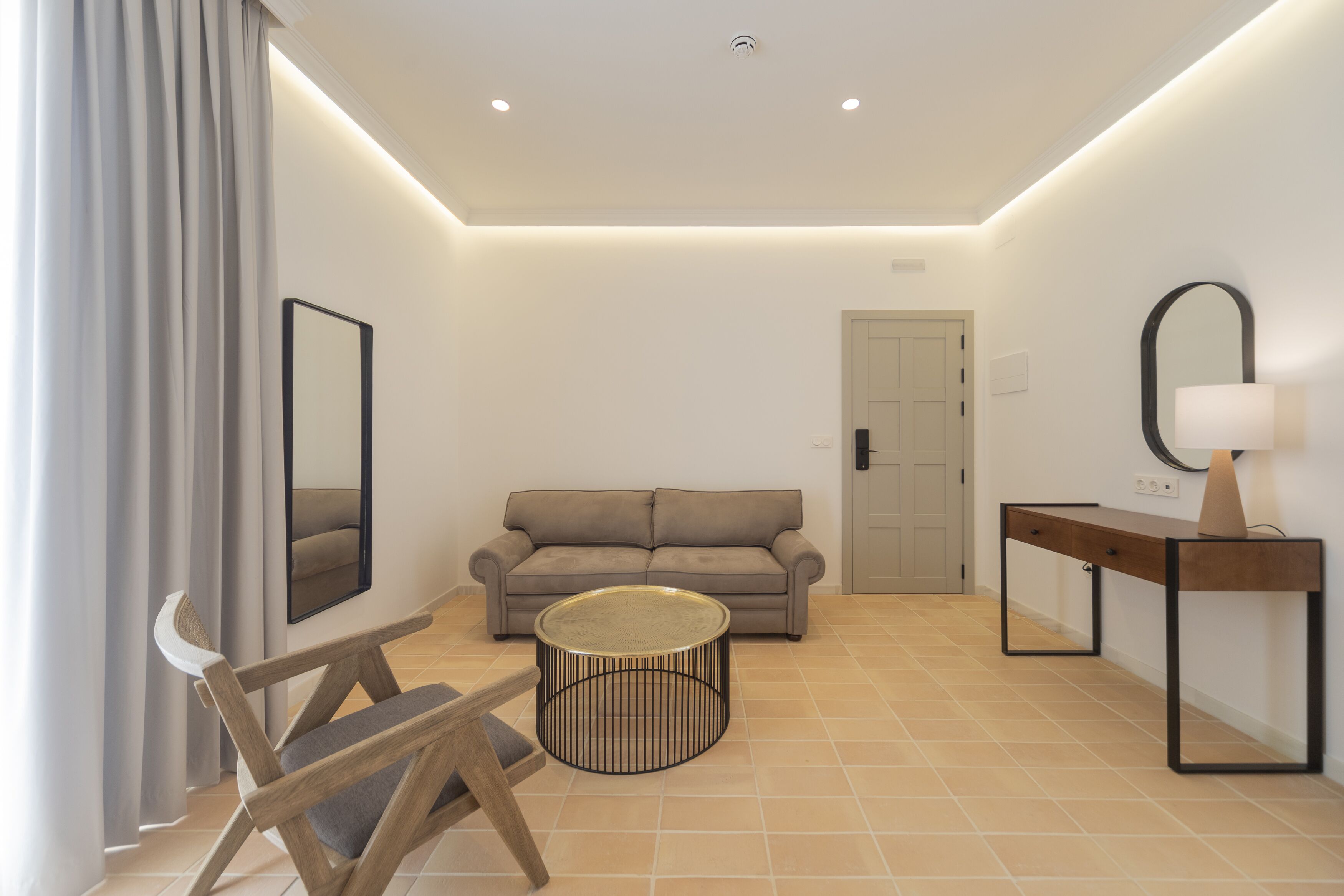 A modern living room with a sofa, a round coffee table, a wooden chair, a side table with a lamp, and a door.