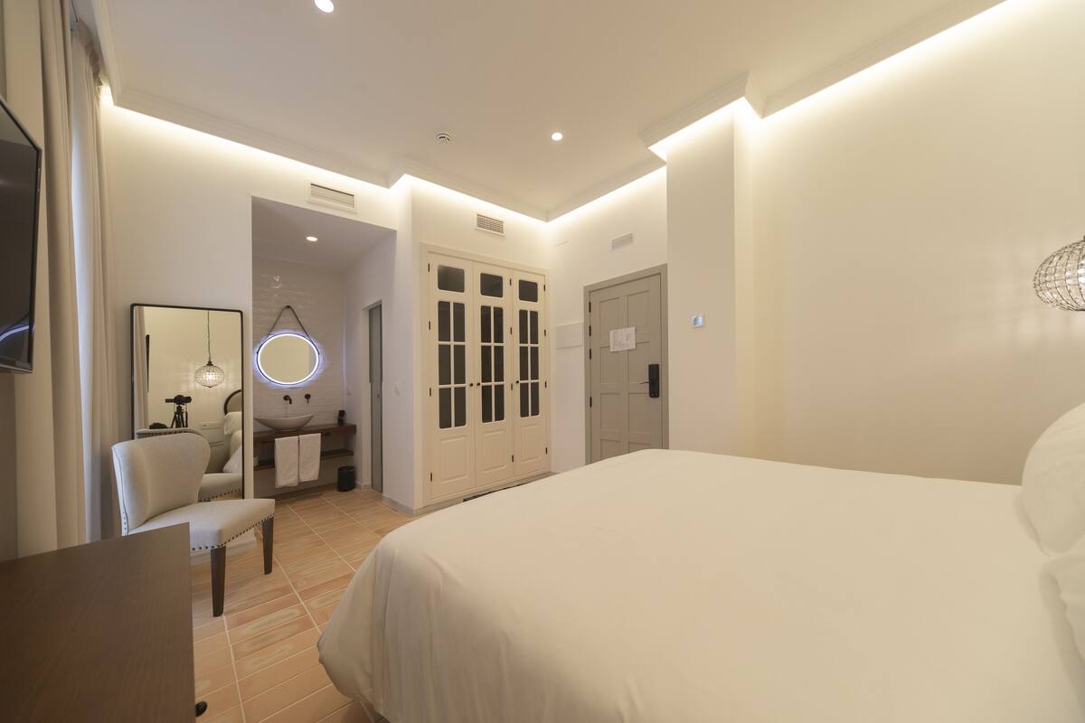 A hotel room with a large bed, a vanity with a mirror, a chair, and a wardrobe.